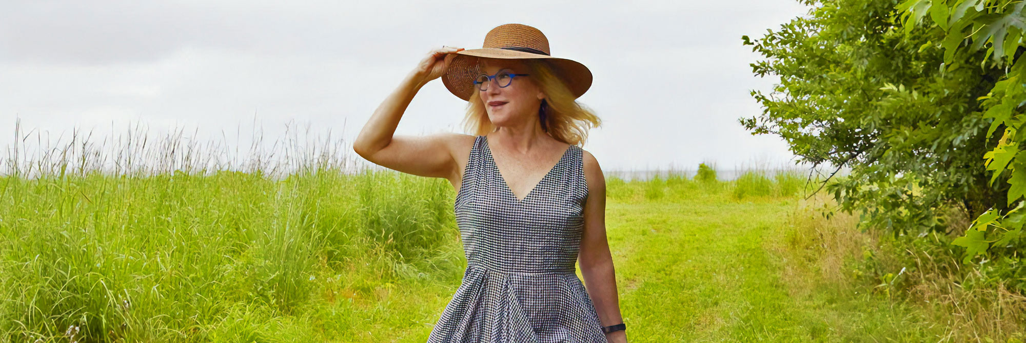 Kara holding a sunhat walking through a field 