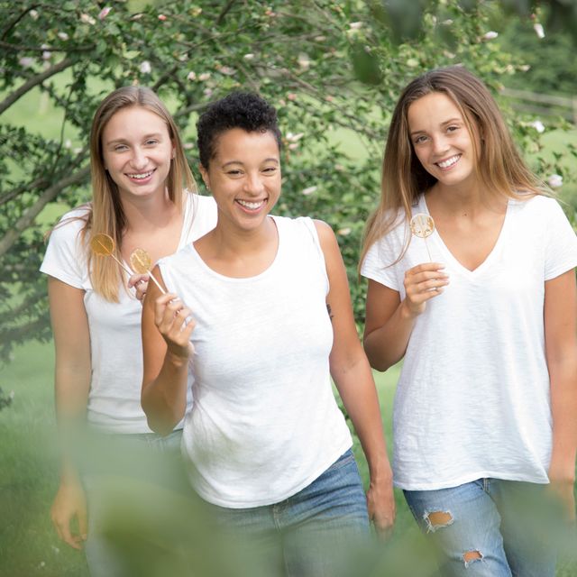 three women walking in nature while holding honey lollipops