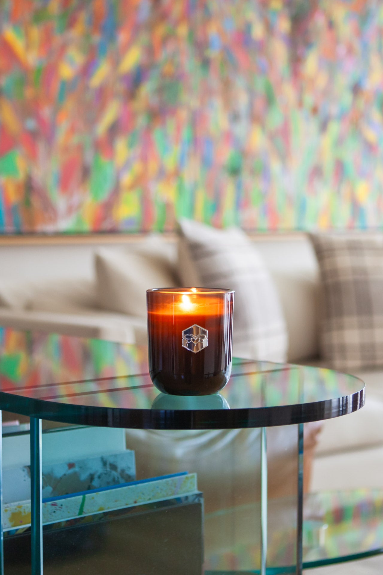 Luxe candle burning on glass table in front of colorful wall 