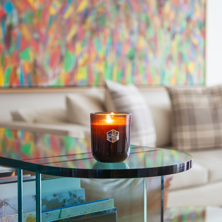 Luxe candle burning on glass table in front of colorful wall 