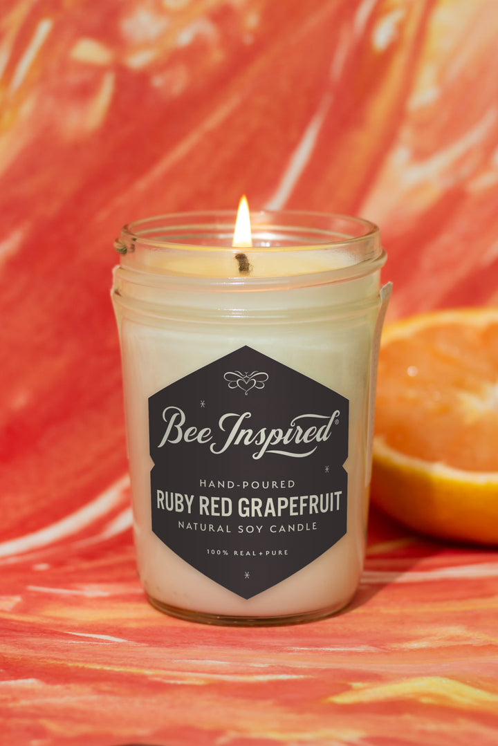 Ruby Red Grapefruit jelly jar candle burning against red and orange art 