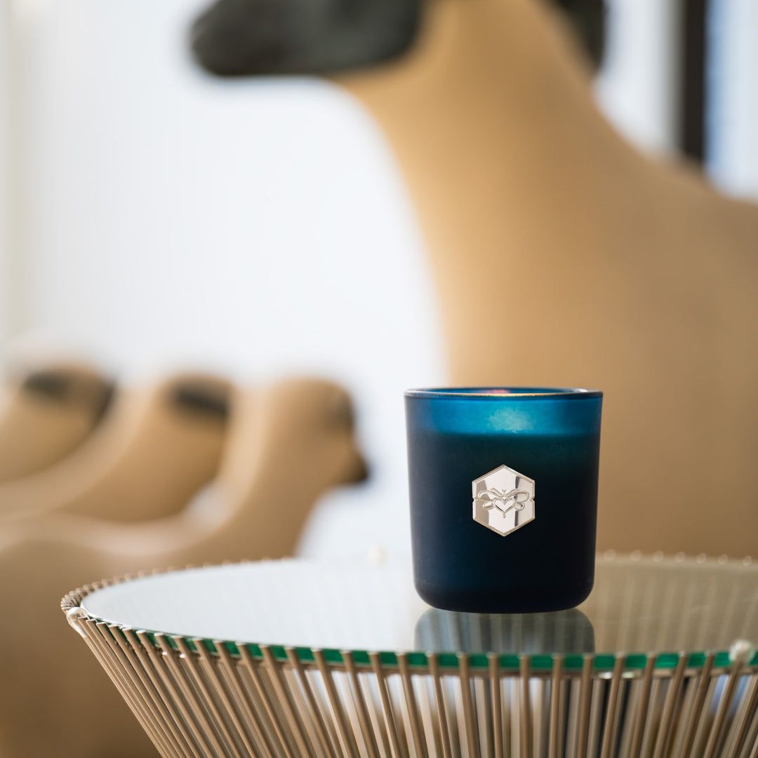 Signature candle on glass table with sheep figurines in background 