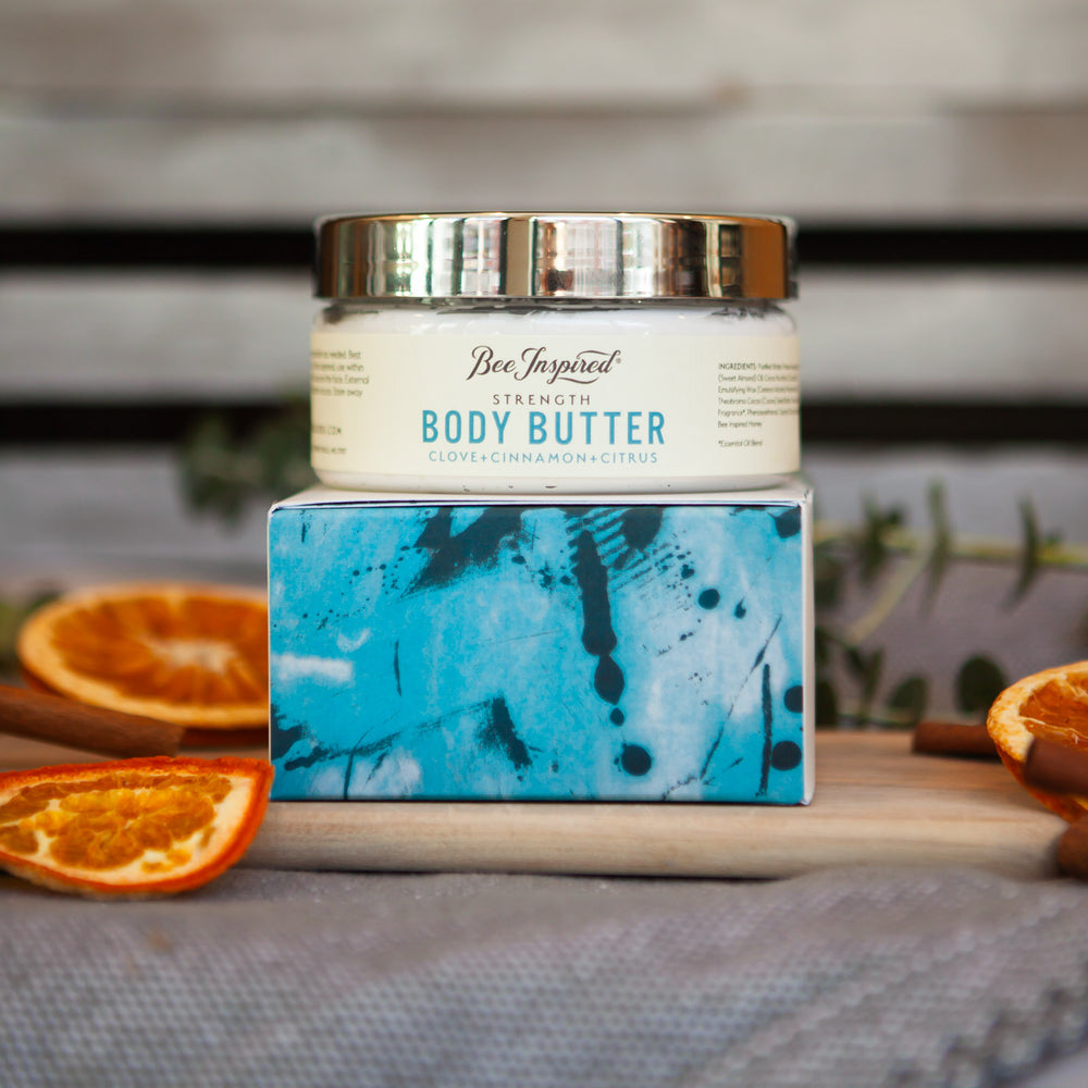 Head on shot of strength body butter on top of body butter box surrounded by orange slices