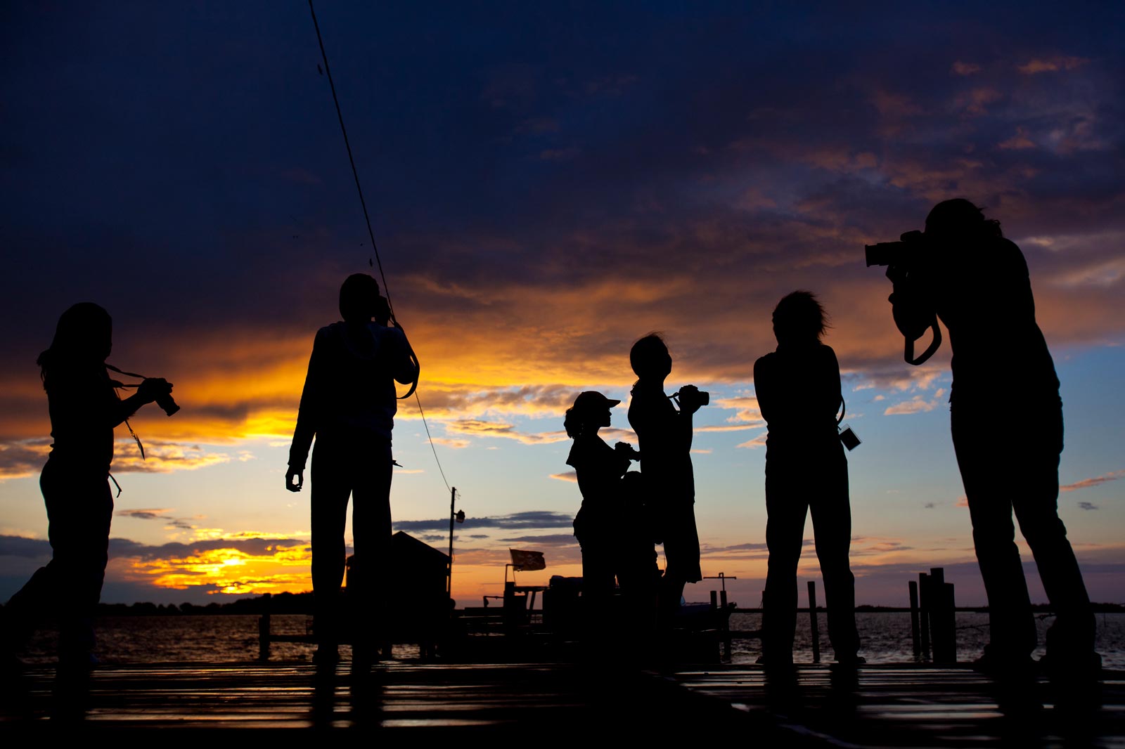 Silhouettes of people on a pier taking pictures of the ocean 