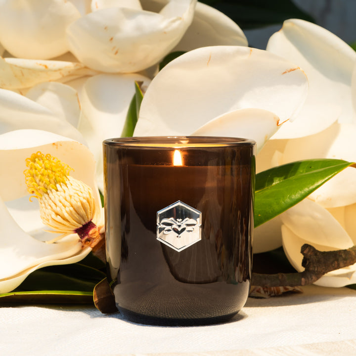 Luxe candle burning in front of white magnolia flowers 