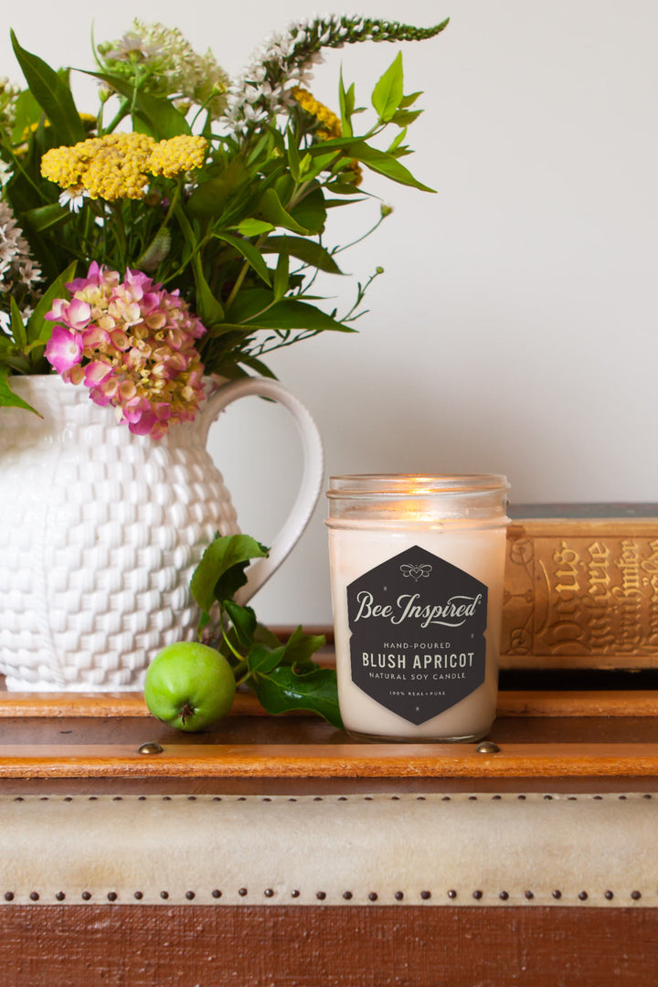 Blush Apricot jelly jar candle burning next to vase of flowers 