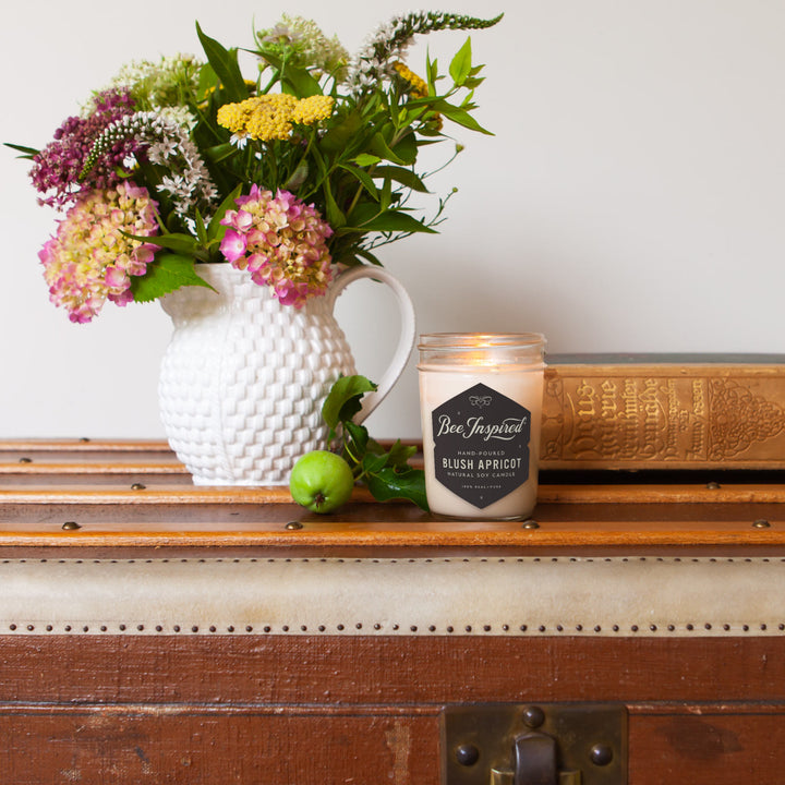 Blush Apricot jelly jar candle burning next to vase of flowers 