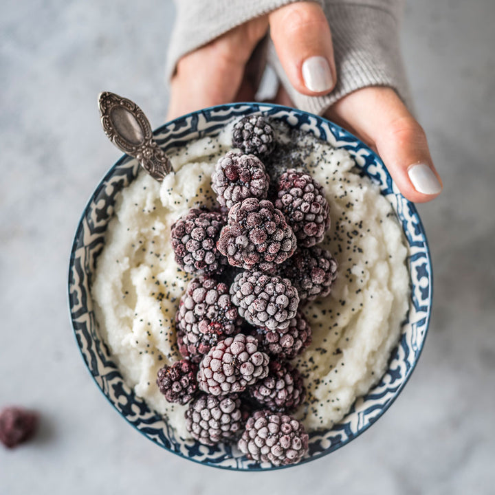 hands holding a bowl of breakfast topped with blackberries