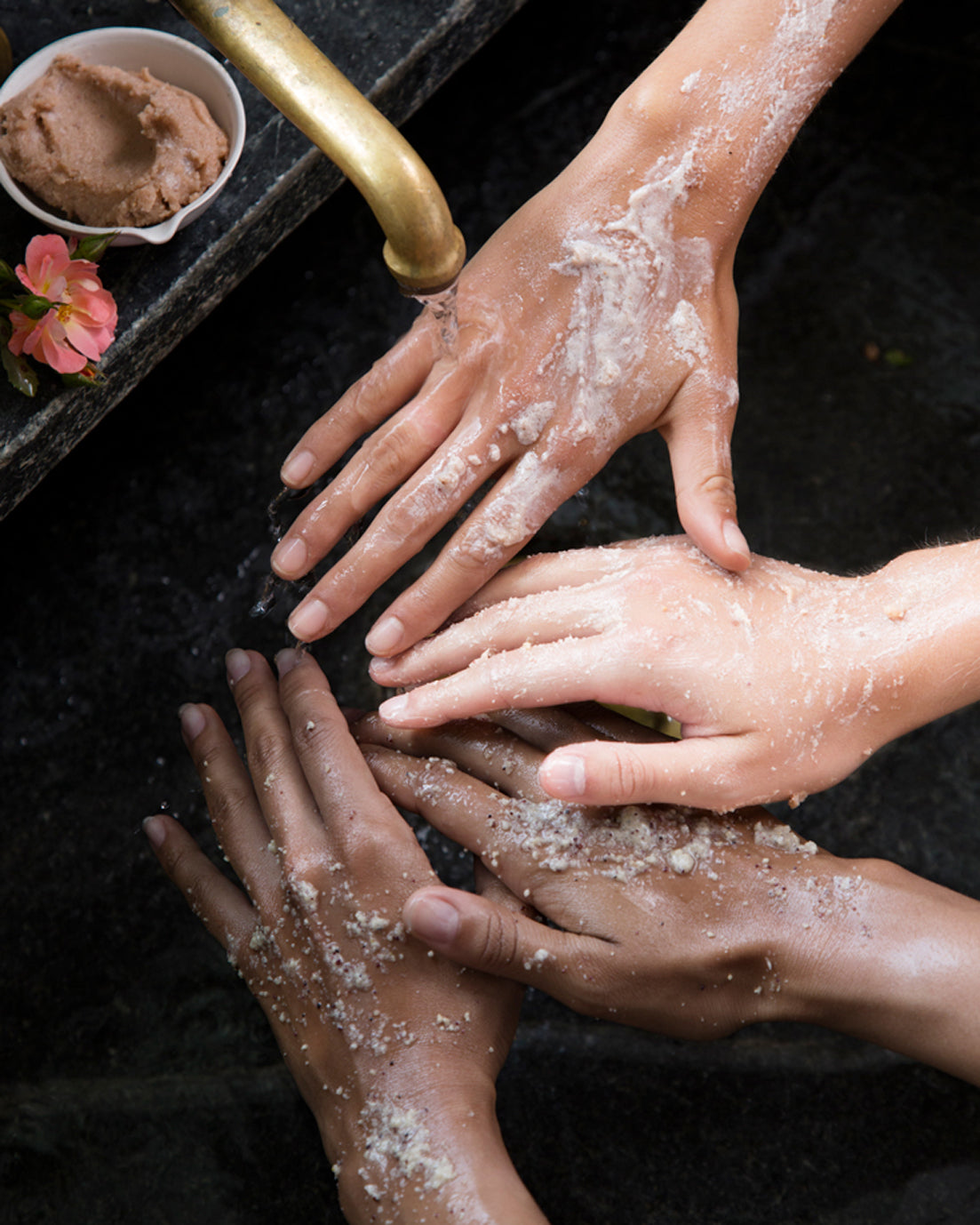 Two people using body scrub on their hands at the sink 