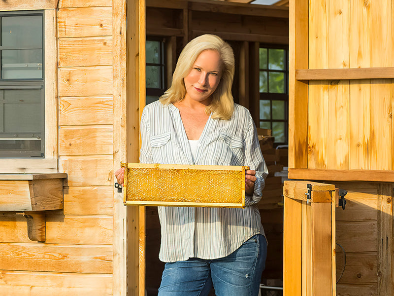 Kara holding a hive frame in doorway of cabin 