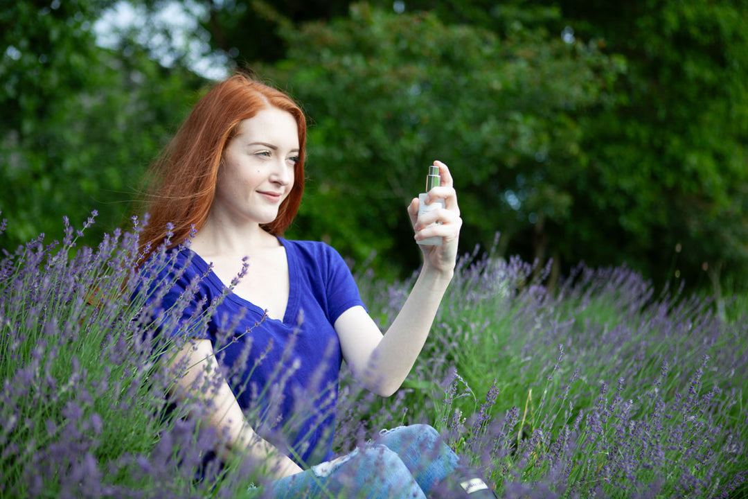 Woman sitting in field of lavender spraying lavender flower water 