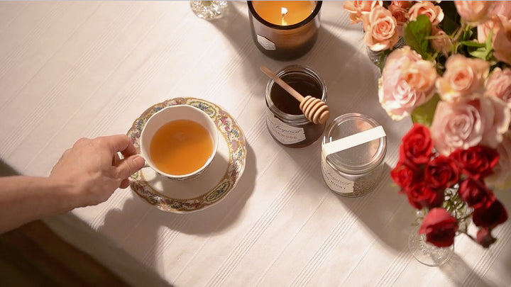 woman holding a cup of tea with honey and tea on a table