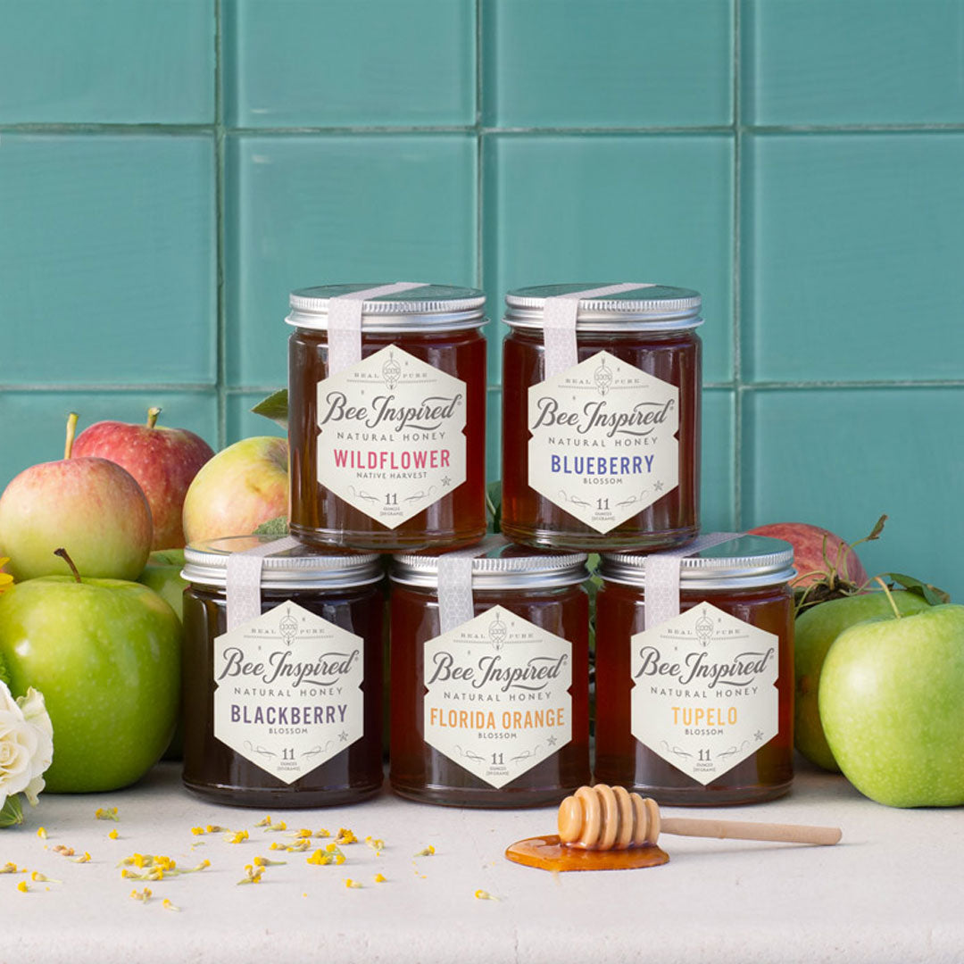 Tower of different honey jars in front of apples 