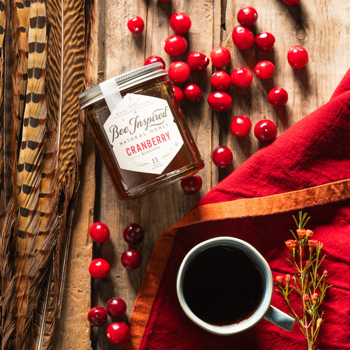 Cranberry honey next to tea mug, cranberries, and feathers 