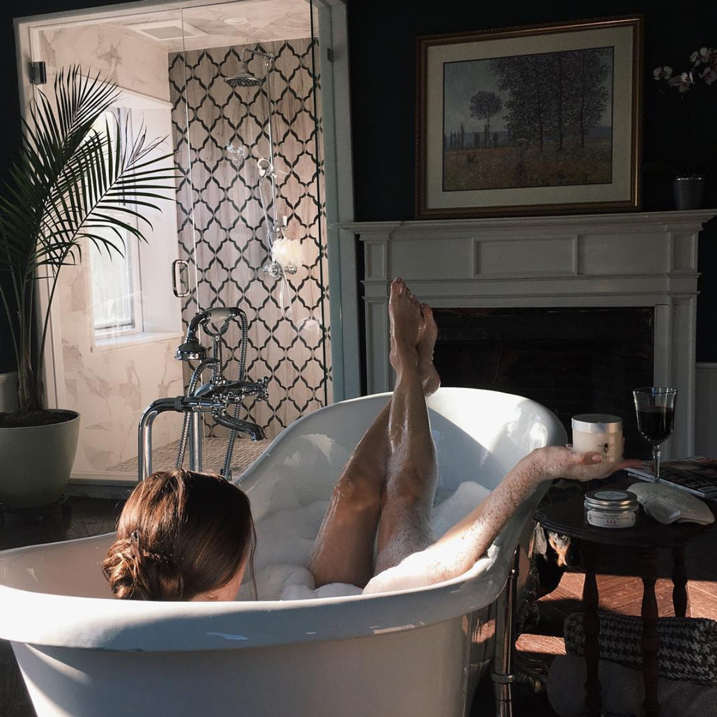 Woman takes a bubble bath with her feet hanging out of the tub 